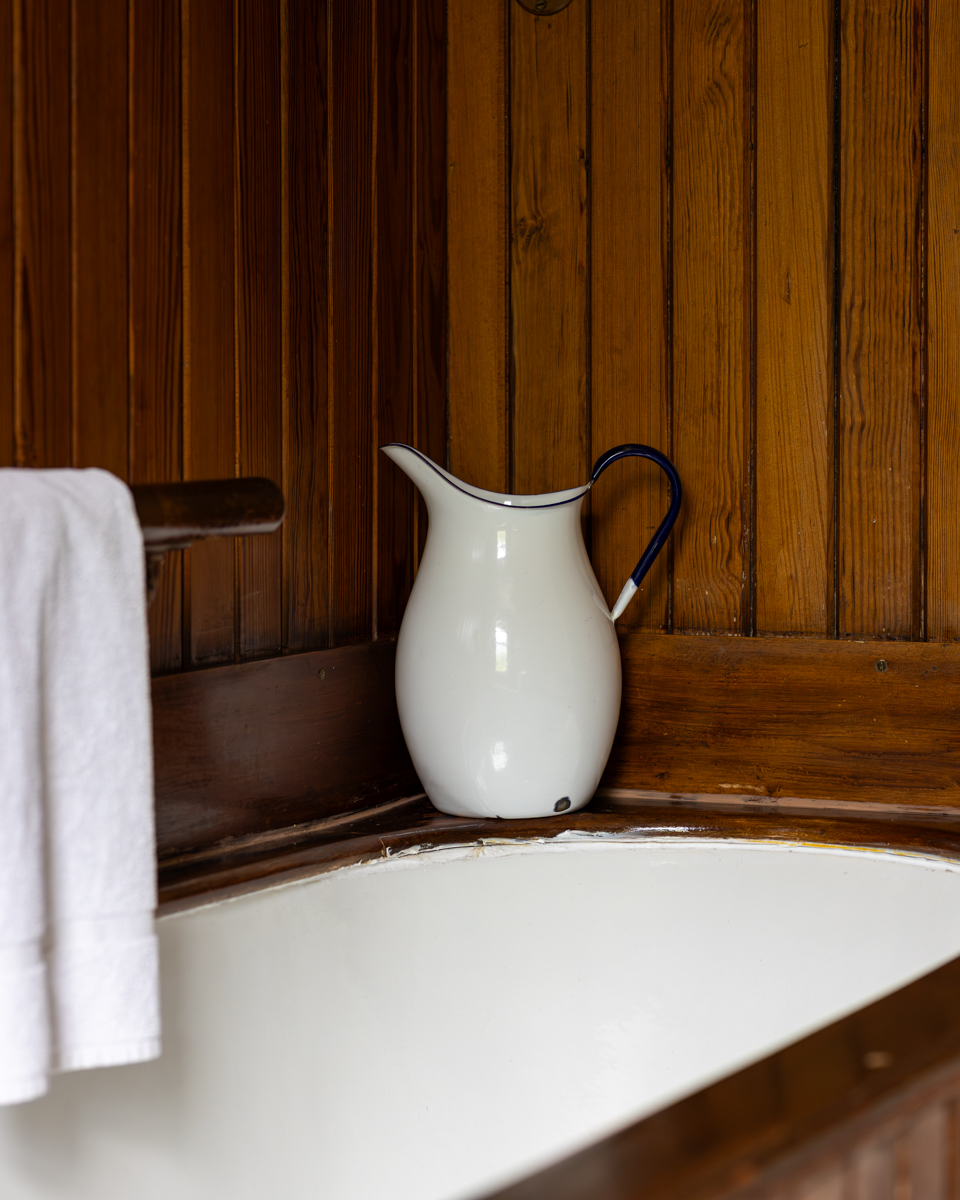 An enamel pitcher resting on a wood-panelled washstand
